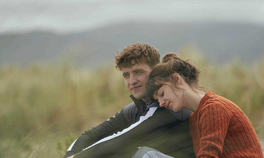 A grey day, tussocky field, a boy and a girl sit close, she resting her head on his shoulder. Both pale and beautiful.