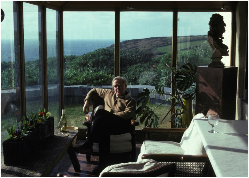 Man relaxes in conservatory with view over cliffs and sea.