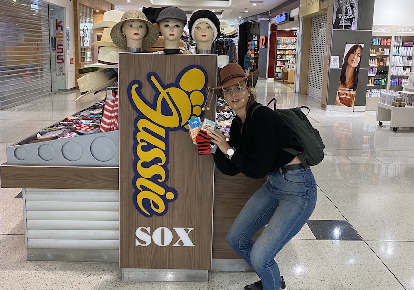 Author squats next to Aussie Sox stall at mall, holding up three pairs of socks.