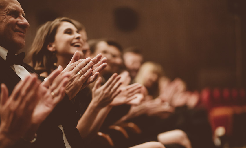 Side view of smiling spectators clapping hands at an awards ceremony.