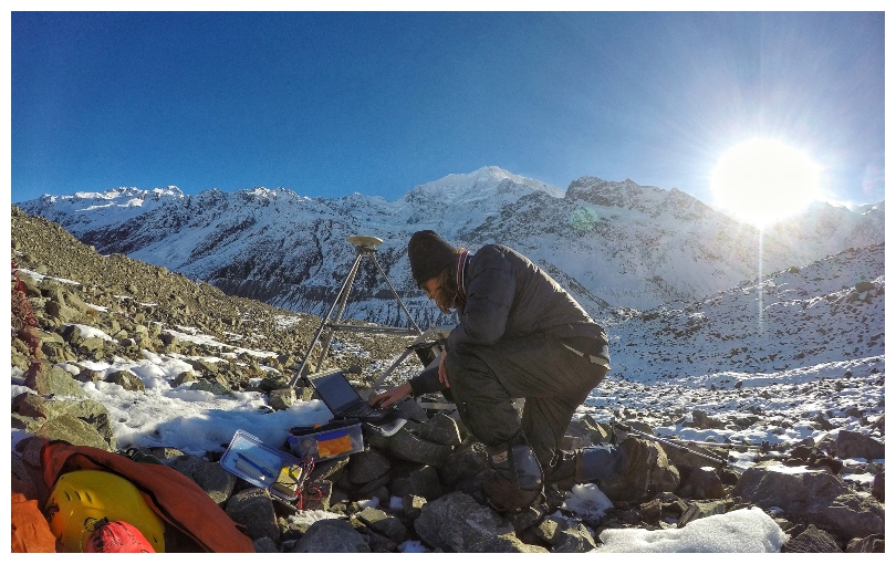 Young man adjusts scientific equipment in the bedrock of the Haupapa glacier. Beautiful clear day.