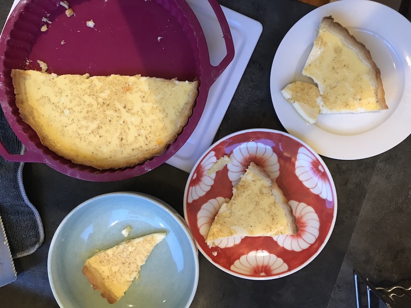 A flan dish with half a custard tart in it, surrounded by plates with wedges of tart.