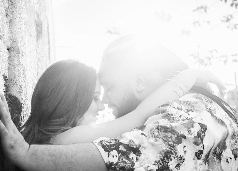 Black and white photograph of a couple, forehead to forehead, of a woman leaning against a tree.  Beautiful light.
