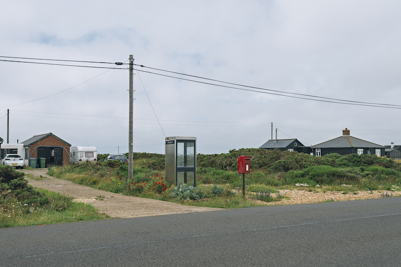 Bleak scene of a road with pebbled driveways, flat horizon, powerlines. Dungeness in the UK.