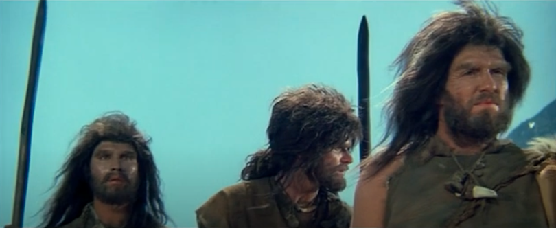 Still from an old film showing three actors dressed as Neanderthals. Terrible wigs.