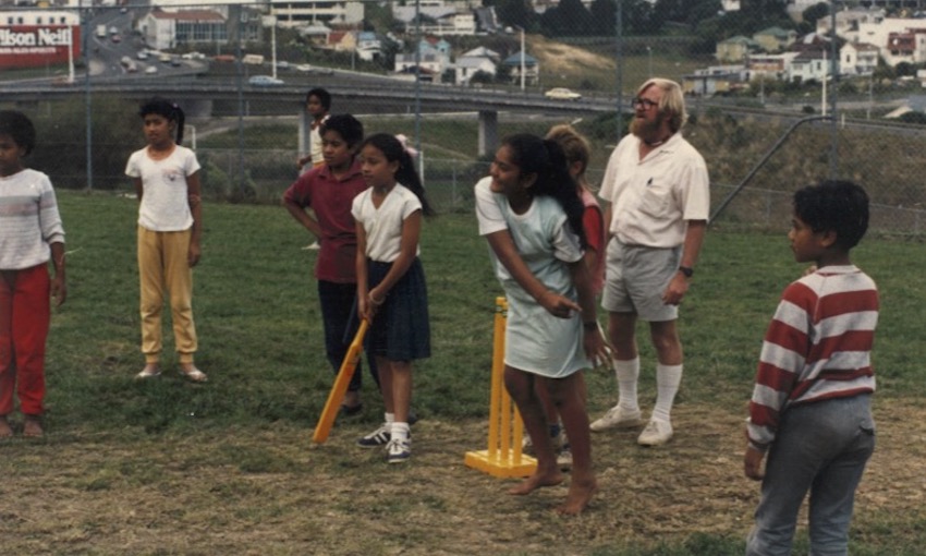 Photo of primary school kids playing cricket with those yellow plastic bat and wickets, a school playing field, a teacher in walk shorts