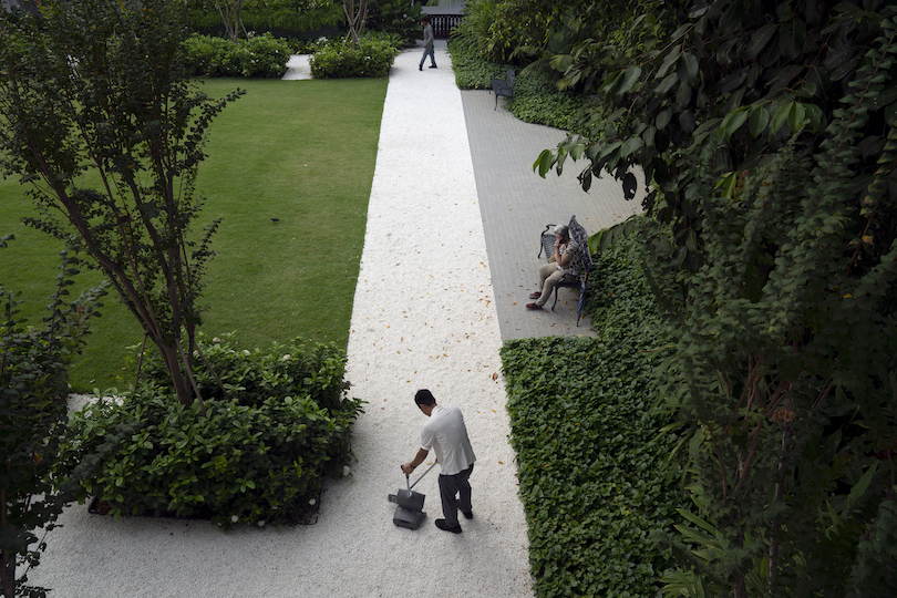 Photo d'un jardin dominé par une allée blanche dont un employé balaie soigneusement les feuilles. 