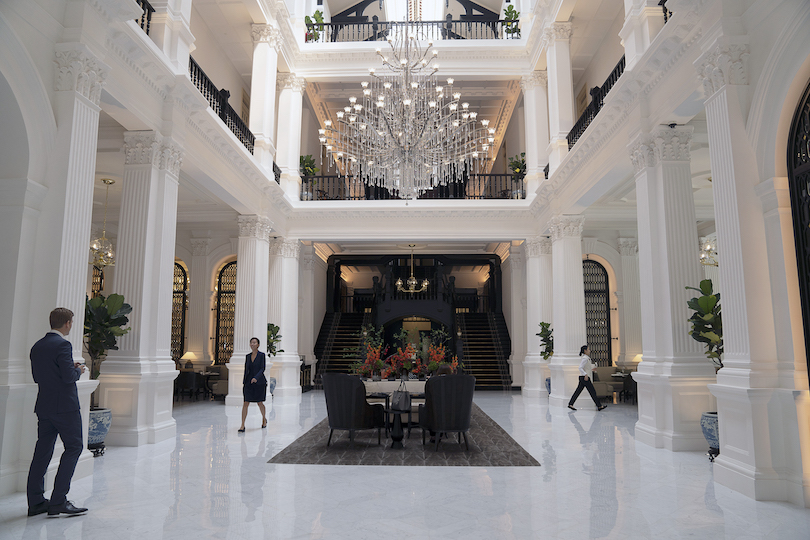 Photo de l'intérieur du hall du Raffles Hotel Singapore – tout est en marbre blanc étincelant et personnel impeccablement habillé, ainsi qu'un lustre